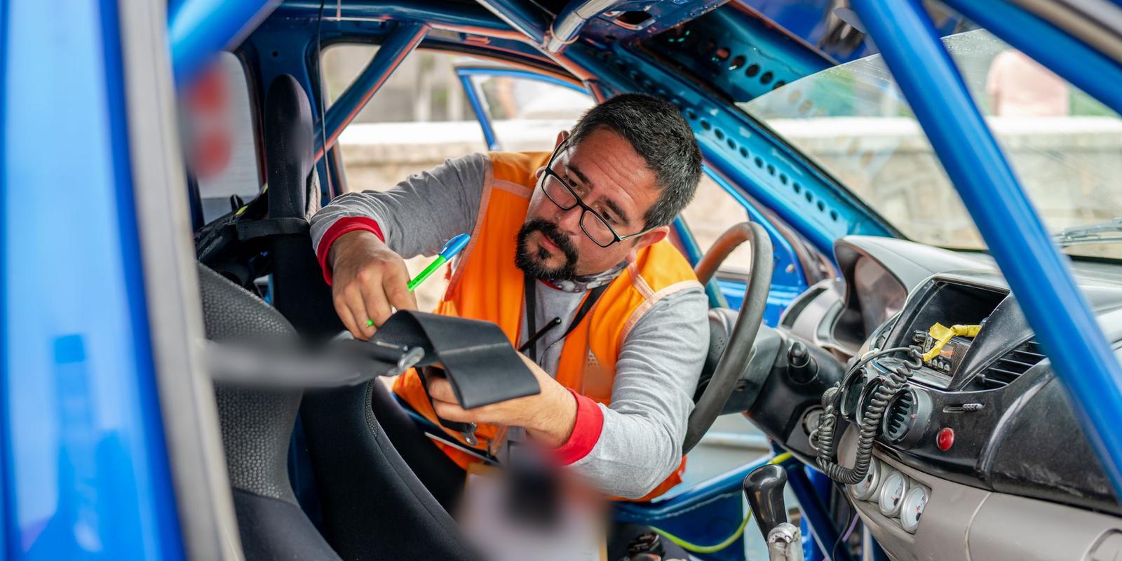 Inspetor de colete laranja examina o cinto de segurança dentro de um carro de competição