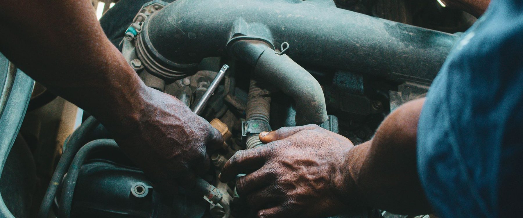 Mãos de mecânico com uma chave soquete ajustando peças no compartimento do motor